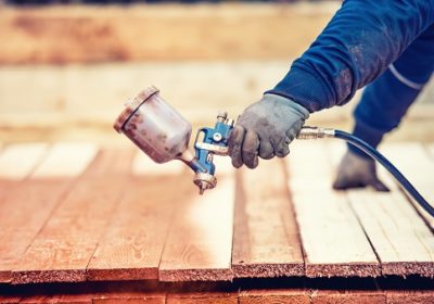 Man using protective gloves painting wooden timber with spray paint gun